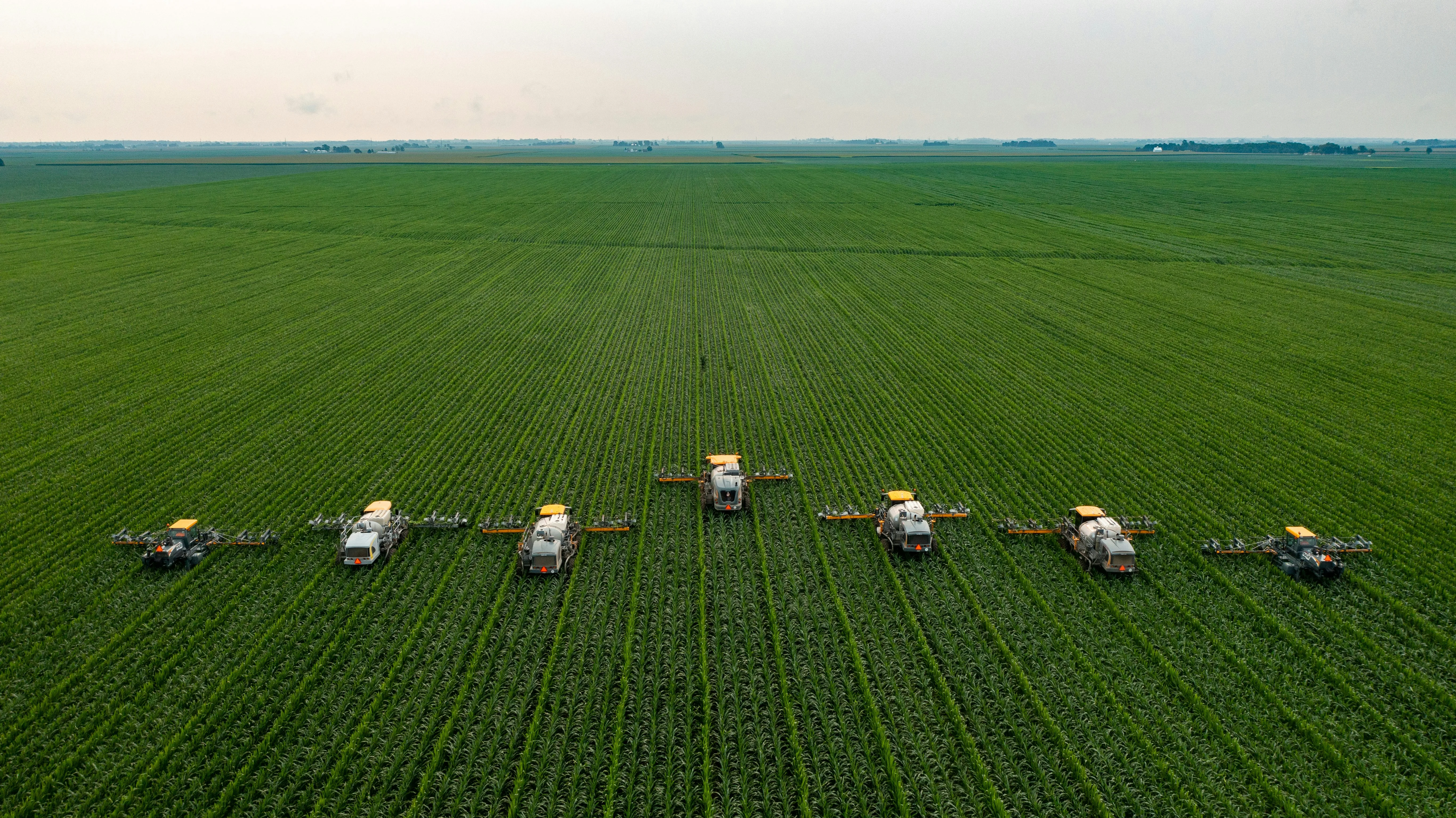 Aerial view of agricultural sprayers in formation across a green crop field