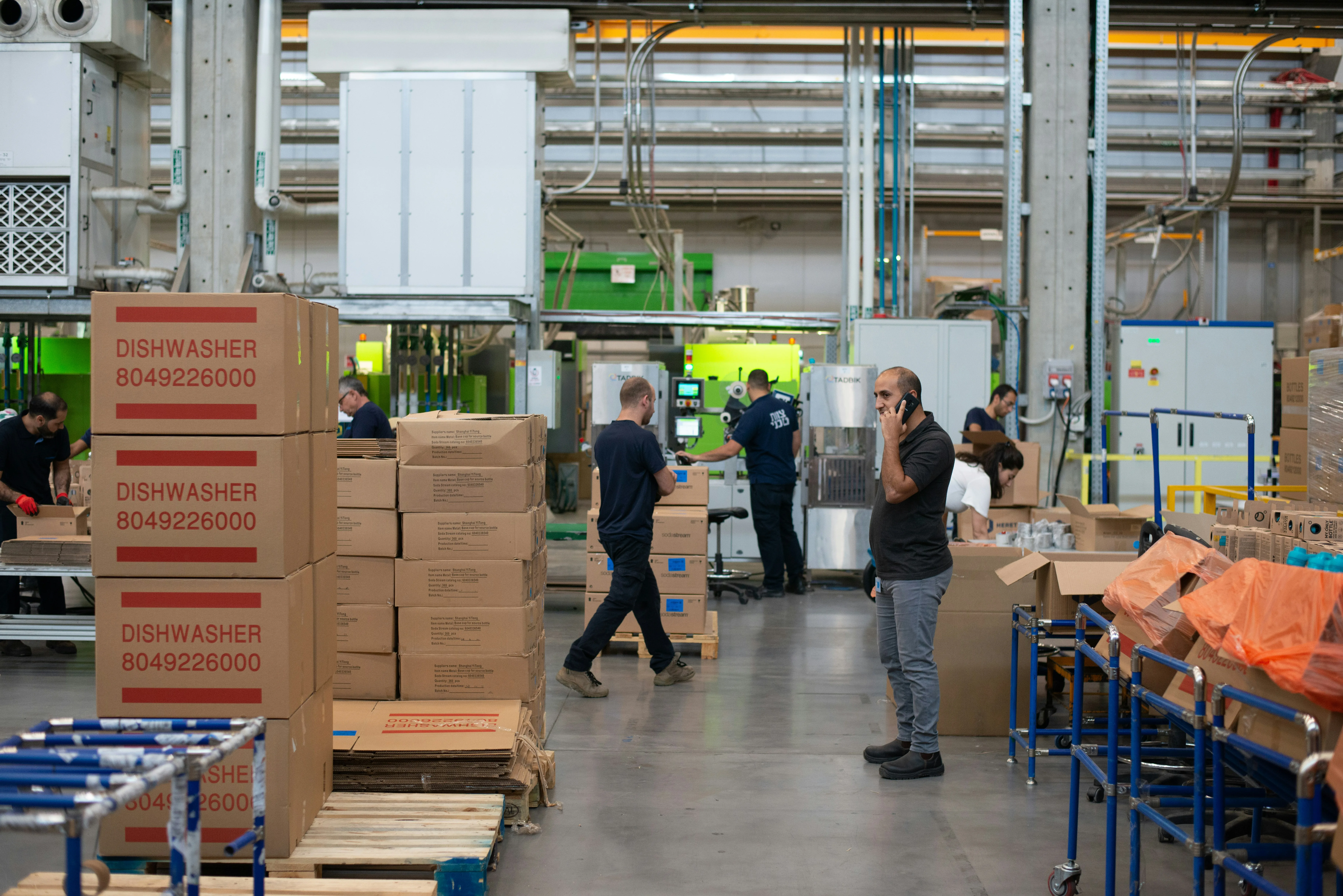 Busy distribution center floor with workers, stacked boxes, and machinery under industrial lighting