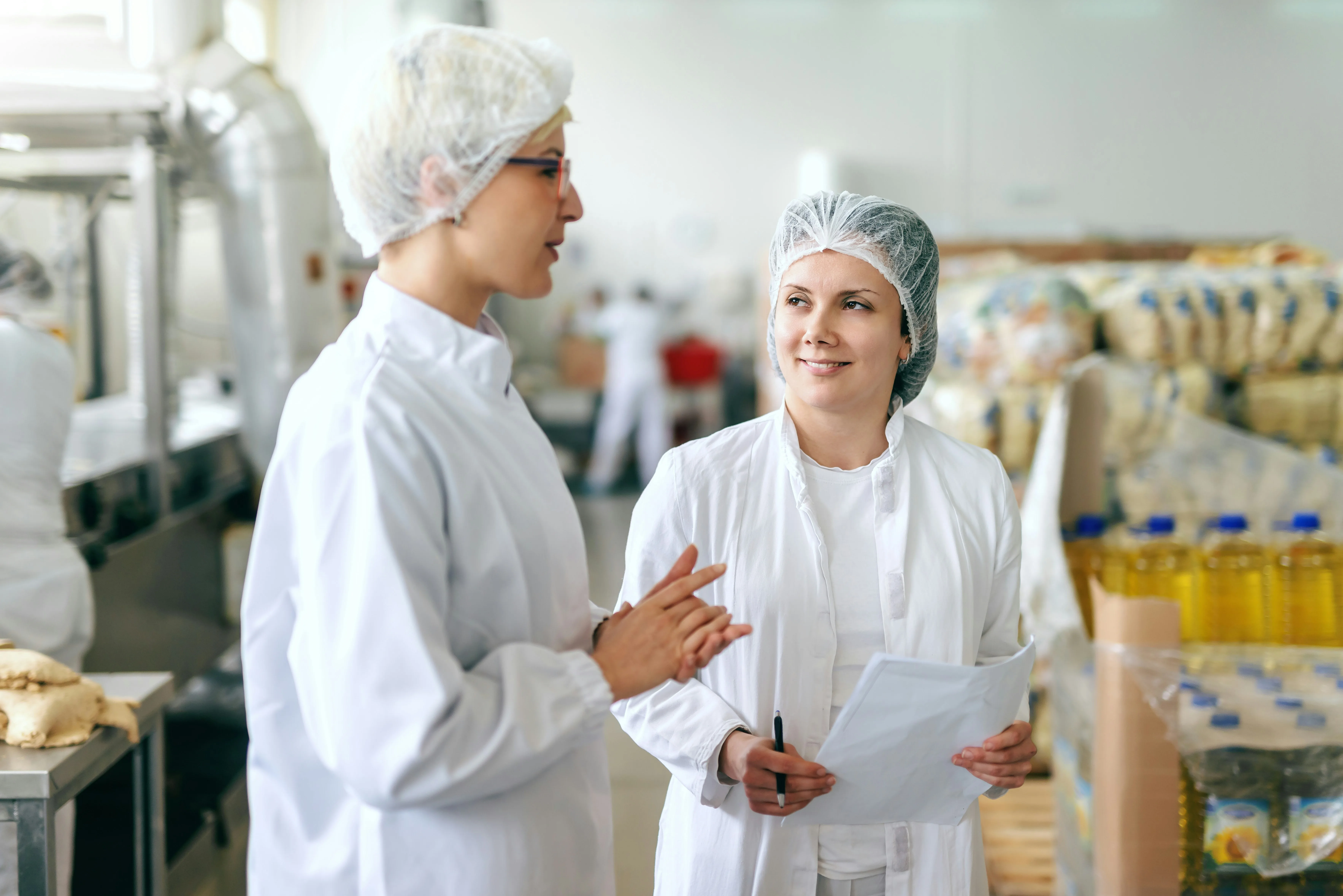 Two food production workers in lab coats discussing operations in a processing facility