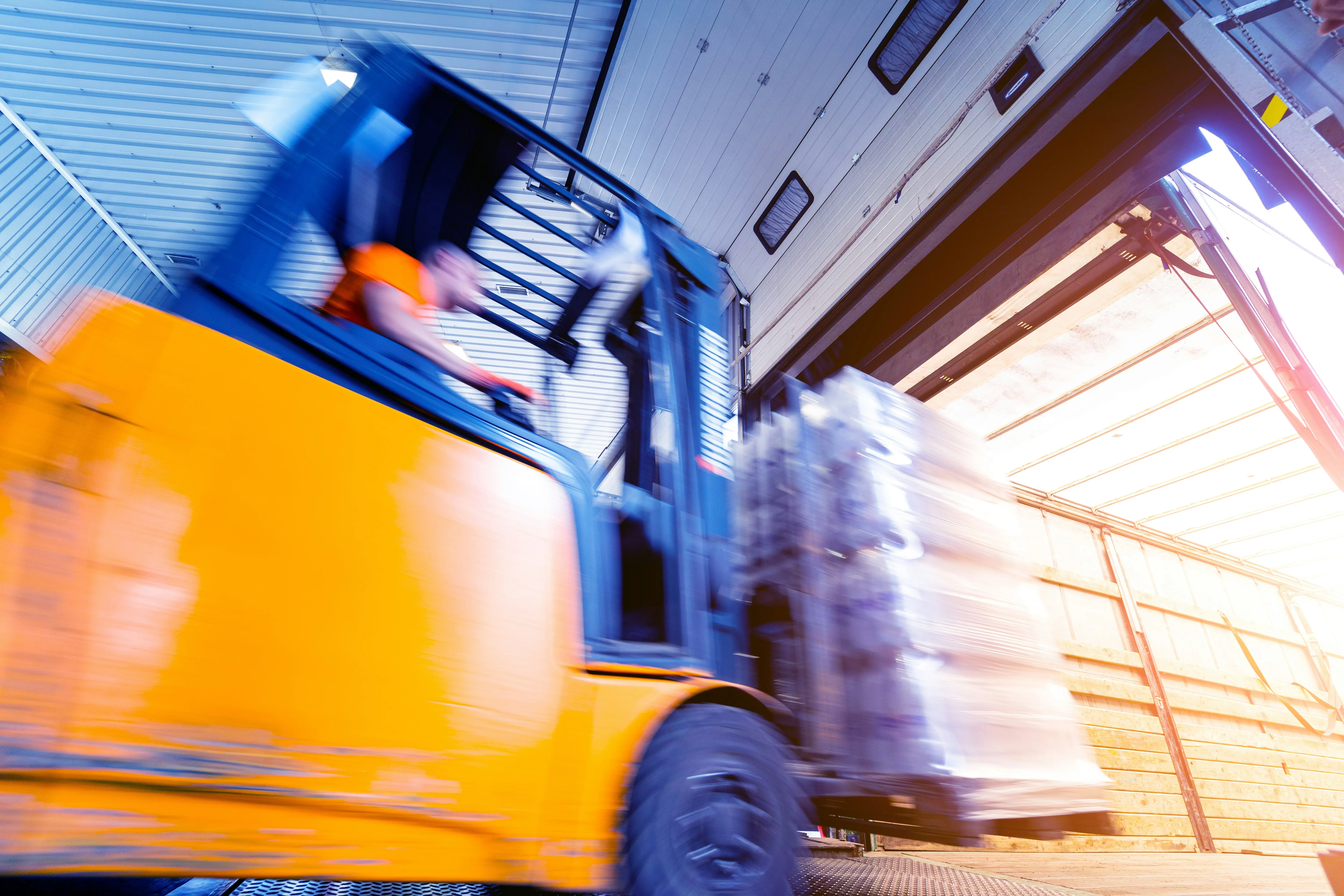 Motion-blurred forklift loading pallets into truck trailer at warehouse dock
