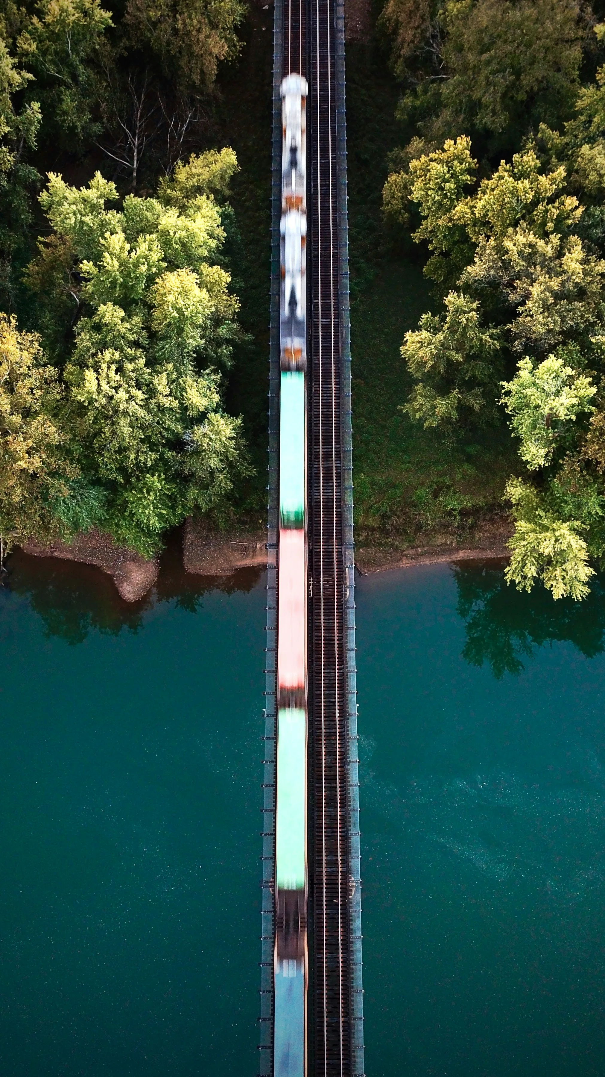 Freight train crossing bridge over turquoise river through forest