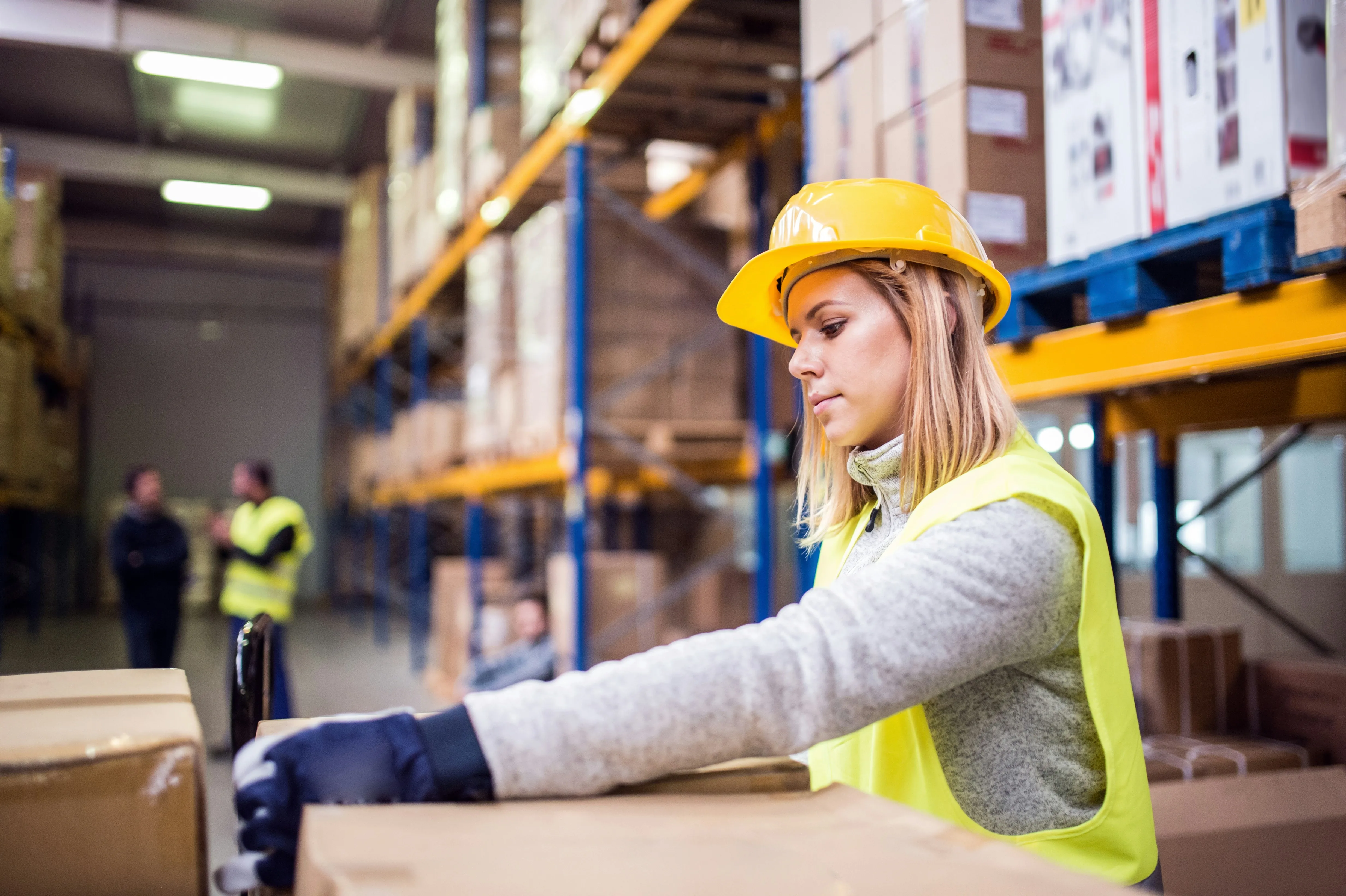Woman in hard hat handling cardboard boxes at packing station in warehouse