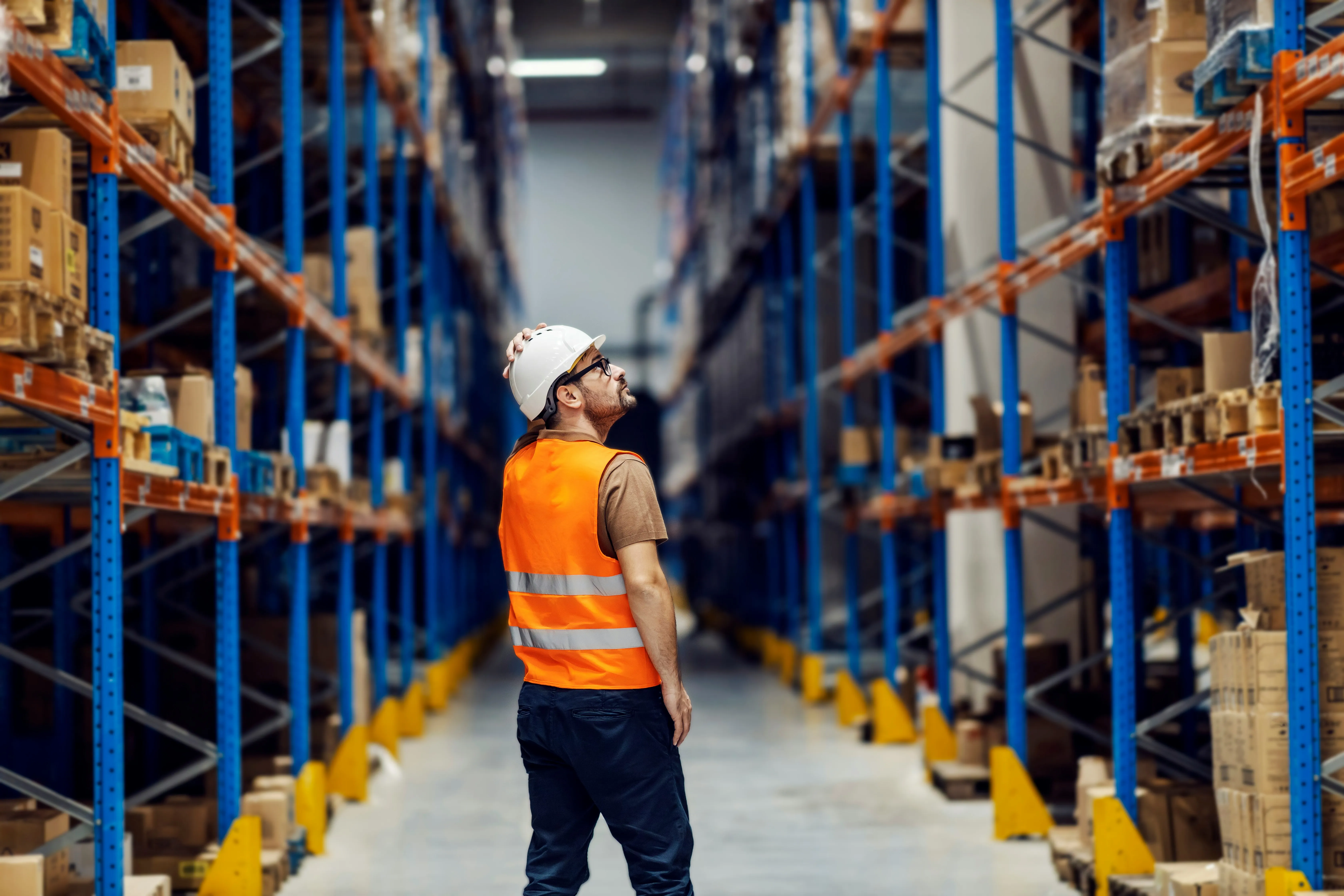 Worker in orange vest standing in tall warehouse aisle